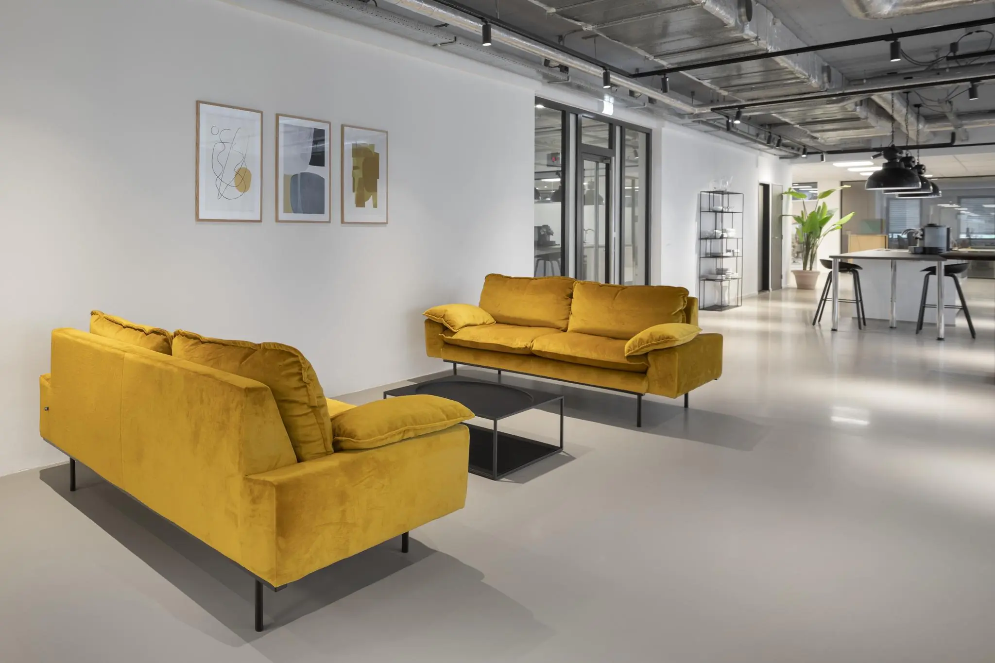 Moderne wachtruimte aan de Van Boshuizenstraat met okergele banken, een zwarte salontafel en minimalistische wandkunst.